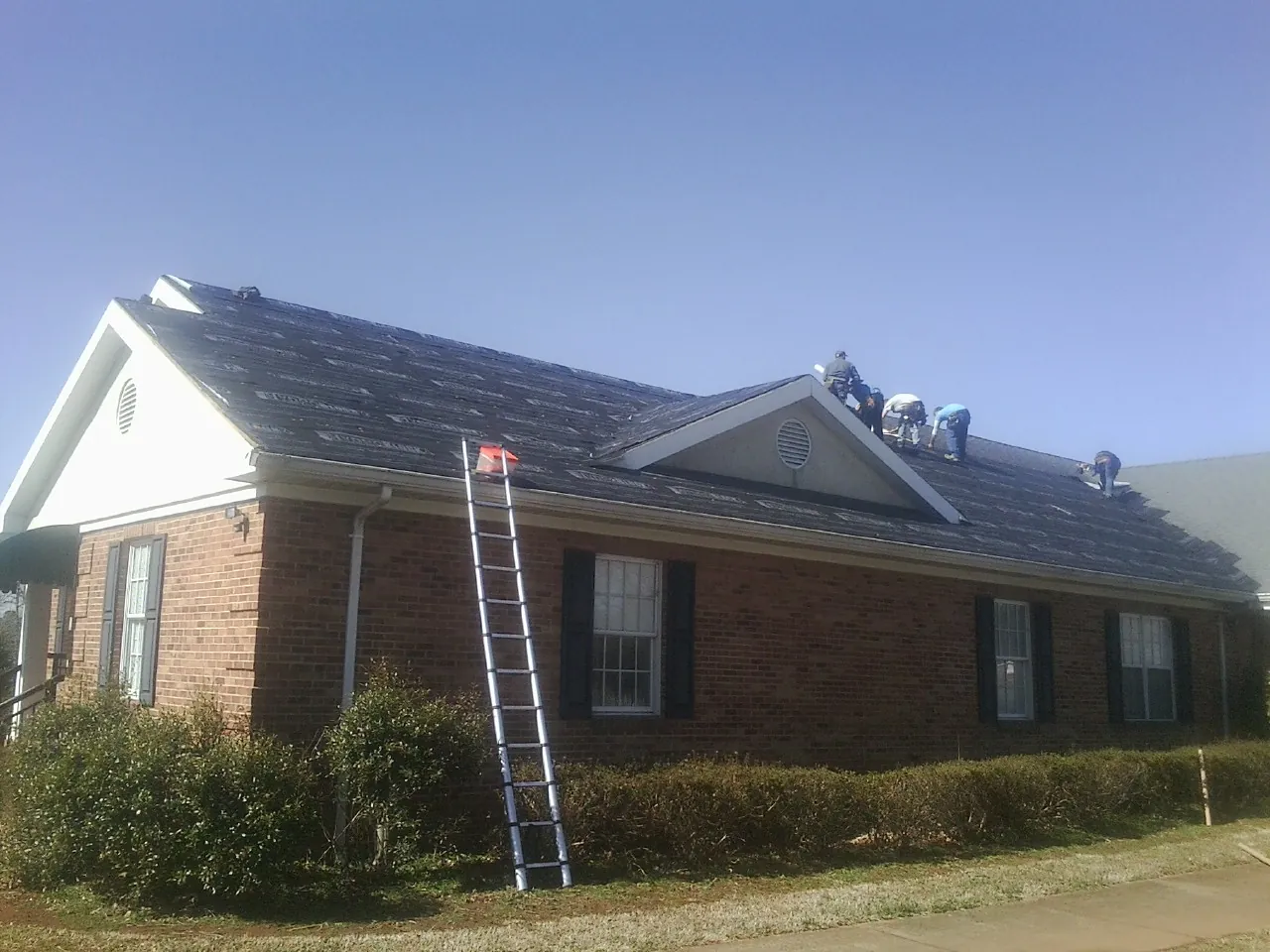 Crew tearing shingles off a brick ranch roof with a ladder set — Emergency Roof Repair work by our crew in West Point