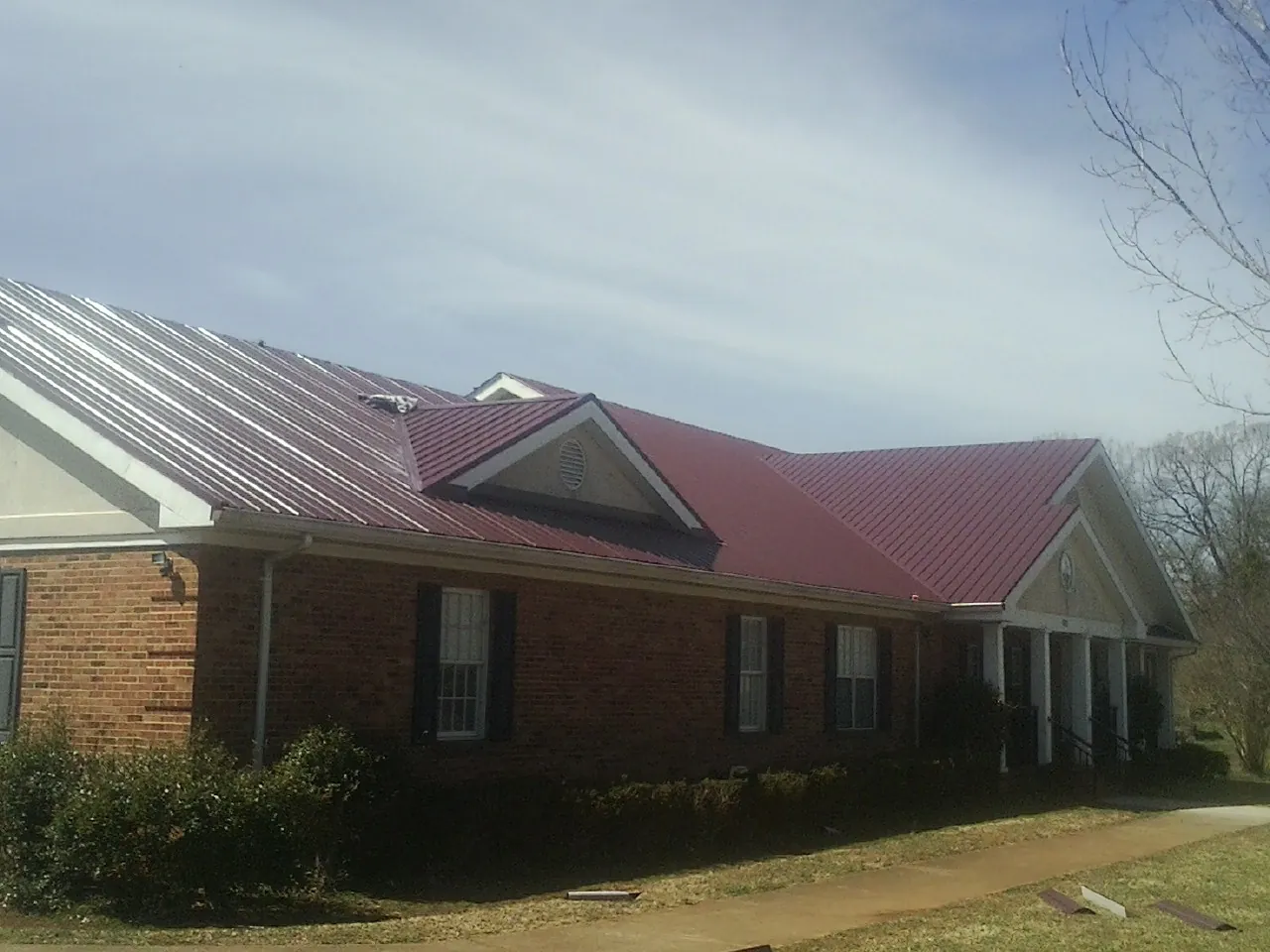 Red metal roof with gabled entries on a long brick building, from a Hail Damage Roof Repair job in West Point
