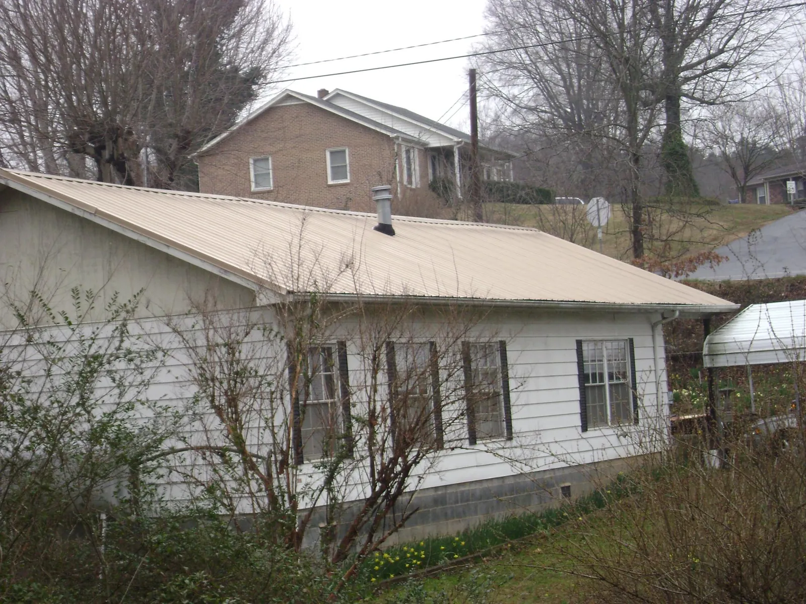 Tan metal roof on a white sided house set into a hillside — Commercial Roofing by Roofing Brothers in West Point